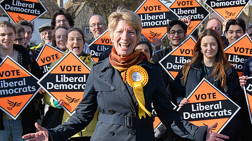 Photo showing Pippa Heylings in front of a large group of Lib Dem supporters holding banners