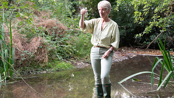 Pippa Heylings, Lib Dem parliamentary candidate for South Cambs, standing in a chalk stream, looking at a test tube full of polluted water