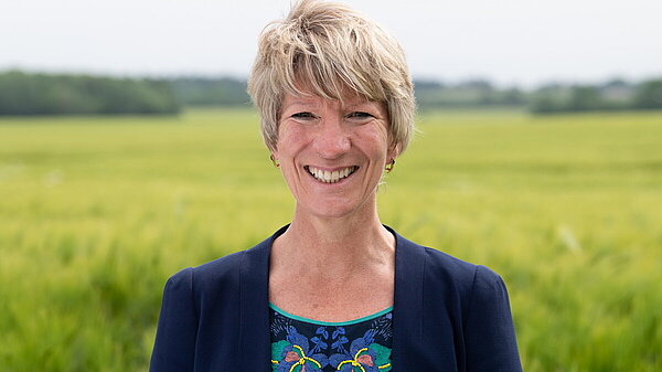 Head and shoulders photo of Pippa Heylings, Lib Dem Parliamentary candidate for South Cambs. Pippa is smiling at the camera, standing in front of a grassy field with trees in the distance.